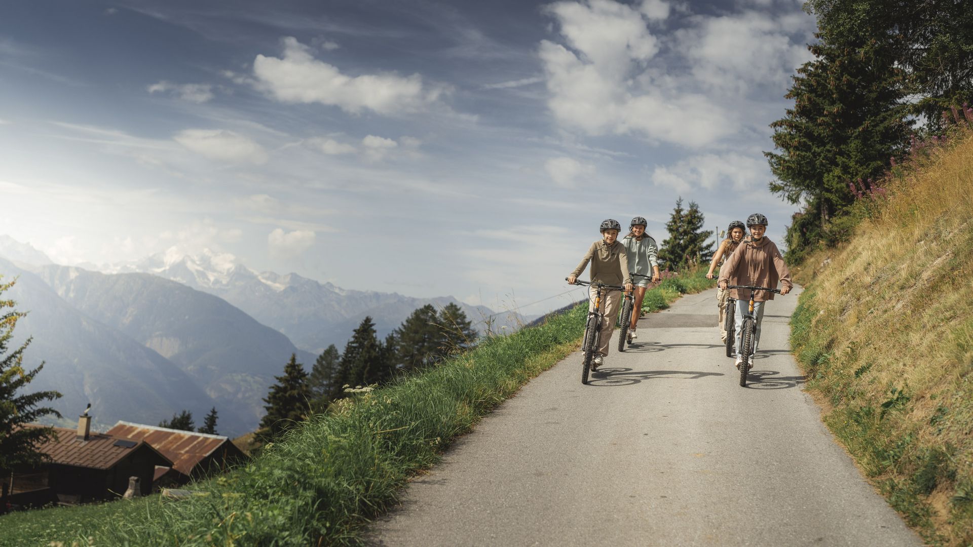 Quatre filles souriantes sur des trottinettes roulent en descente, un super complément au Mountaincart Aletsch Arena.