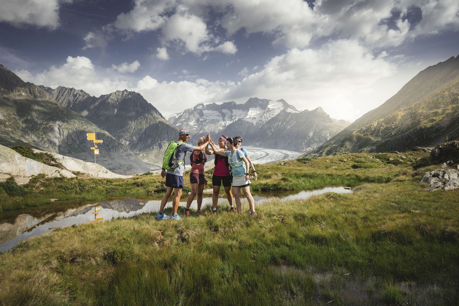 Vier Trailrunner beim High-Five vor dem Grossen Aletschgletscher und beeindruckender Bergkulisse in der Aletsch Arena.