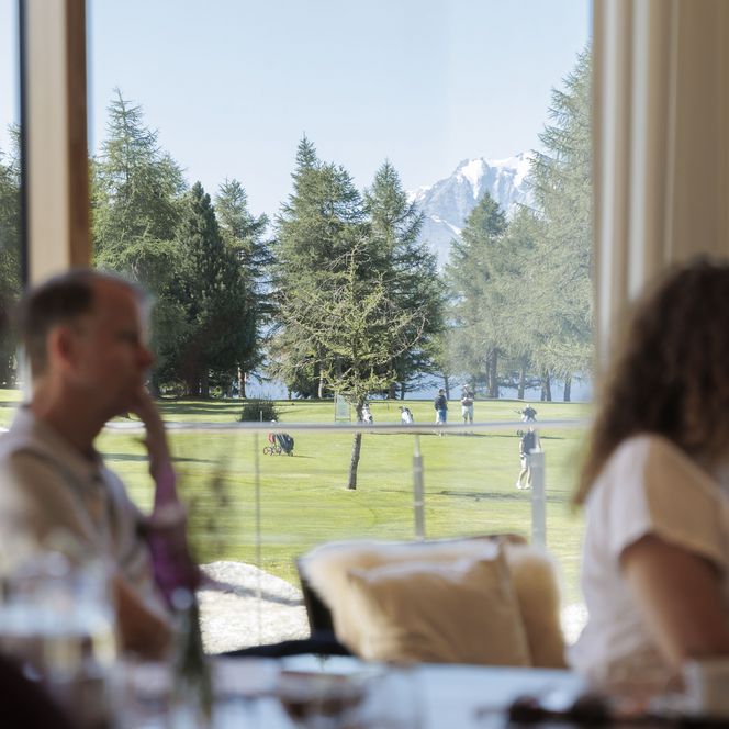 Teilnehmer von einem Retreat Aletsch Arena sitzen am Tisch und blicken durch ein Fenster auf Berge und Wiesen.