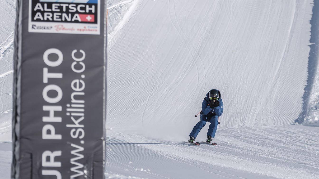 Ein Skifahrer fährt dynamisch eine präparierte Piste auf der Fiescheralp hinunter und passiert gleich dabei einen Skiline-Fotopunkt in der Aletsch Arena.