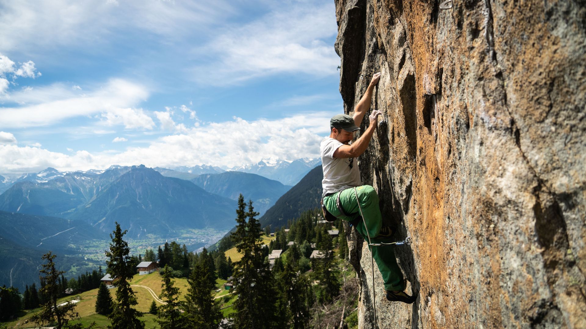 Un grimpeur escalade une paroi rocheuse du site d'escalade « Adler » et découvre les joies de l'escalade dans l'Aletsch Arena, face à un panorama montagneux impressionnant.