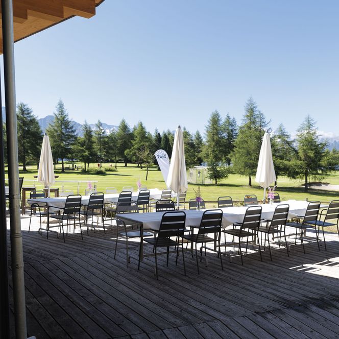Eine Holzterrasse mit weiss gedeckten Tischen, draussen vorbereitet für die Teilnehmer vom Retreat Aletsch Arena.