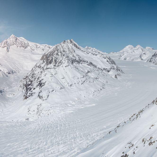 In winter, the Great Aletsch Glacier rests deep in snow under a white blanket of snow between high mountain peaks.