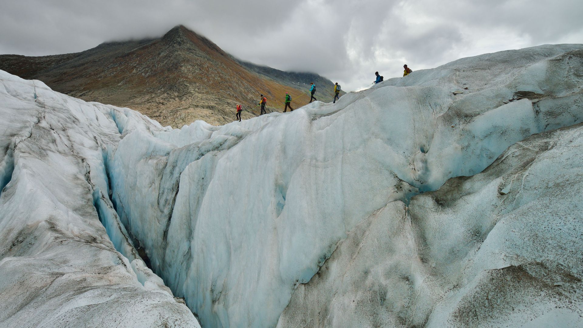 A roped-up group hikes very carefully along the edge of a deep crevasse on the Aletsch Arena glacier tour.