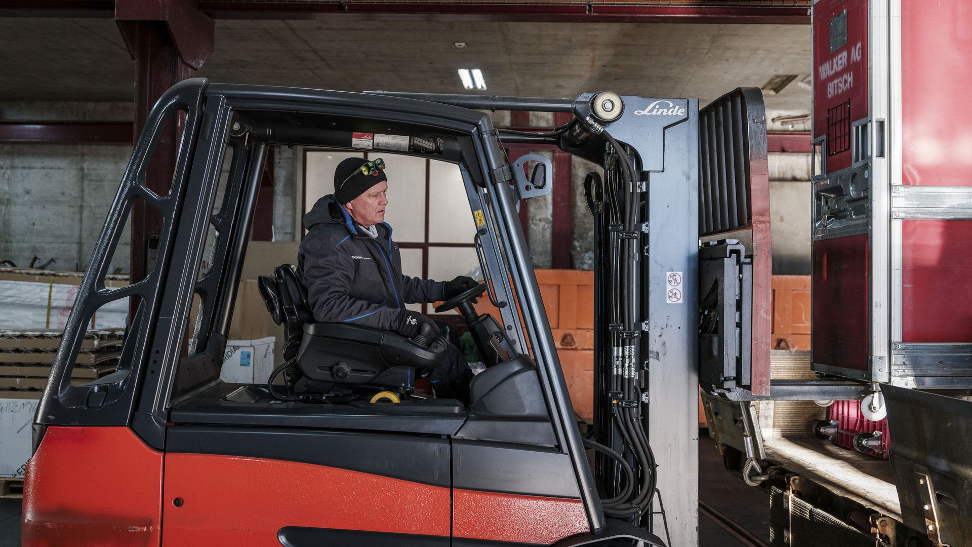 Jobs Aletsch Bahnen AG: Person bedient einen roten Gabelstapler beim Güterverlad neben einer Transportkabine.