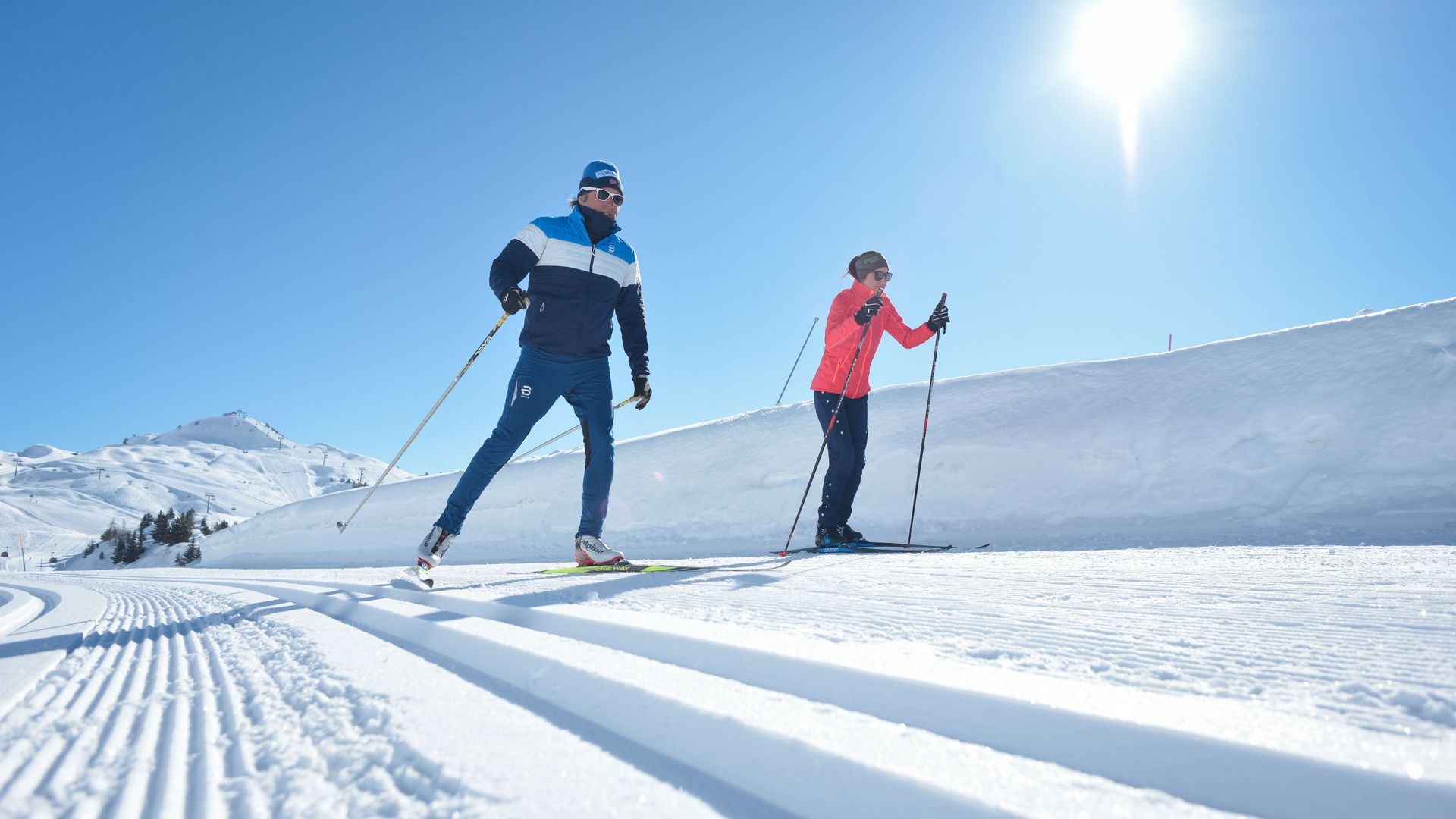 Deux sportifs pratiquant le ski de fond dans l'Aletsch Arena, sur une piste fraîchement damée, sous un ciel d'un bleu éclatant.