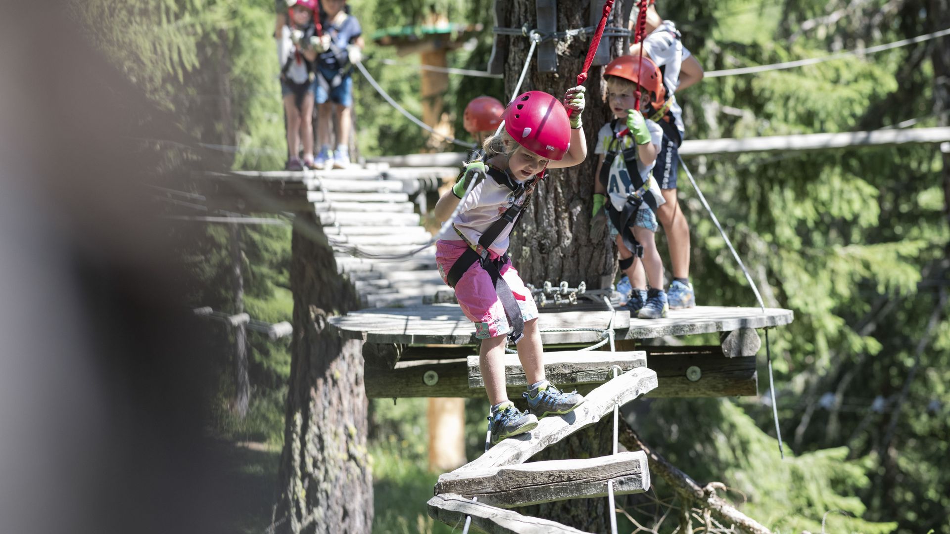 Équipés de casques et de baudriers, les enfants franchissent des obstacles au parc d'accrobranche de Baschweri et découvrent de près l'escalade dans l'Aletsch Arena.