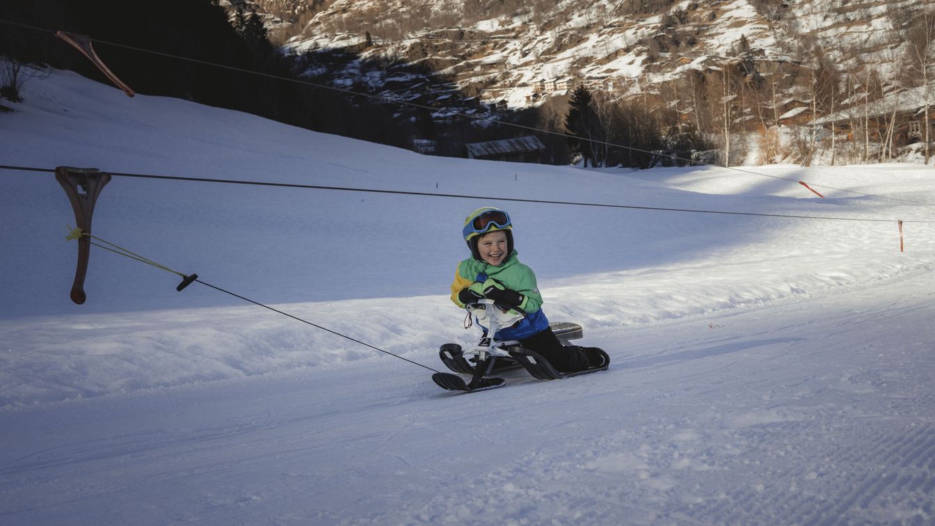 Ein Junge sitzt auf einem Snowbike und wird vom Skilift Blätz im Fieschertal den verschneiten Hang hinaufgezogen.