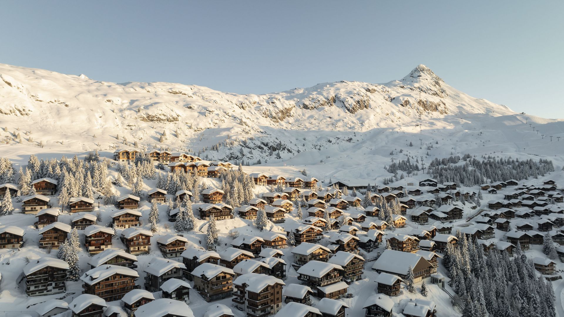 Luftaufnahme der tief verschneiten Holzchalets auf der Bettmeralp Schweiz mit markantem Berggipfel im Hintergrund.