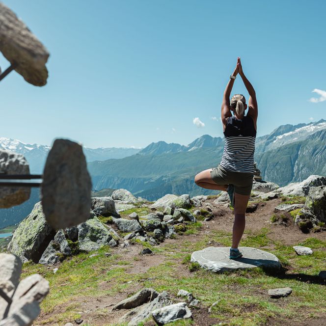 Eine Frau praktiziert Yoga am Kraftort Harmonie auf der Bettmerhorn und blickt über die Berglandschaft der Aletsch Arena.