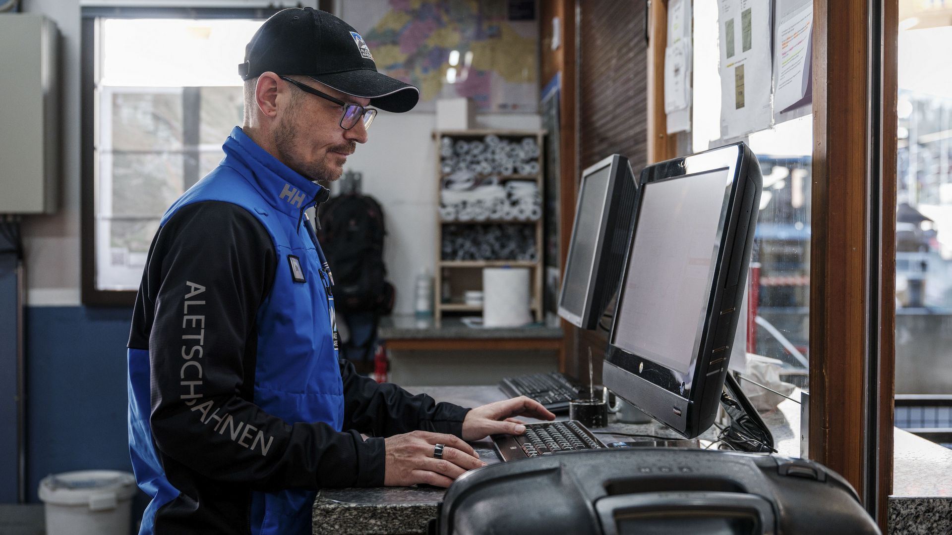 Jobs Aletsch Bahnen AG: Person in Arbeitskleidung bedient den Computer am Ticketverkaufsschalter.