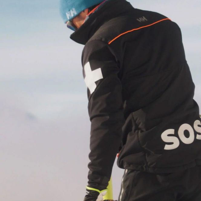 Jobs Aletsch Bahnen AG: Person der Pistenrettung mit SOS-Jacke und gelber Stange in verschneiter Umgebung.
