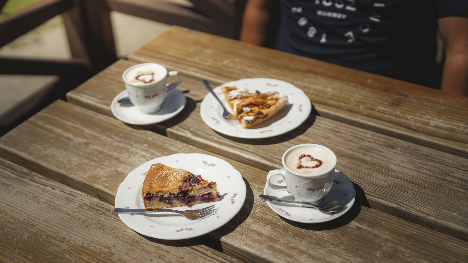 Zwei Kaffee und frischer Kuchen auf einem Holztisch bei der Villa Cassel in der Aletsch Arena an einem sonnigen Tag.
