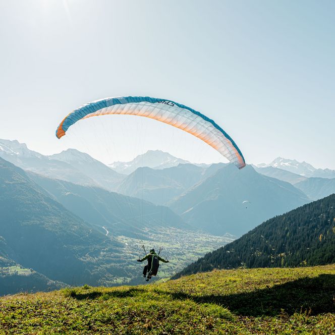 Gleitschirmflieger beim Start auf grüner Bergwiese hoch über dem weiten Alpental und Bergen