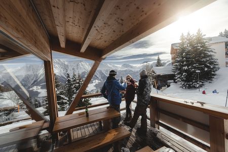 Eine Gruppe stösst im Winter auf einer Holzterrasse mit Bergsicht nach einem Retreat Aletsch Arena an.