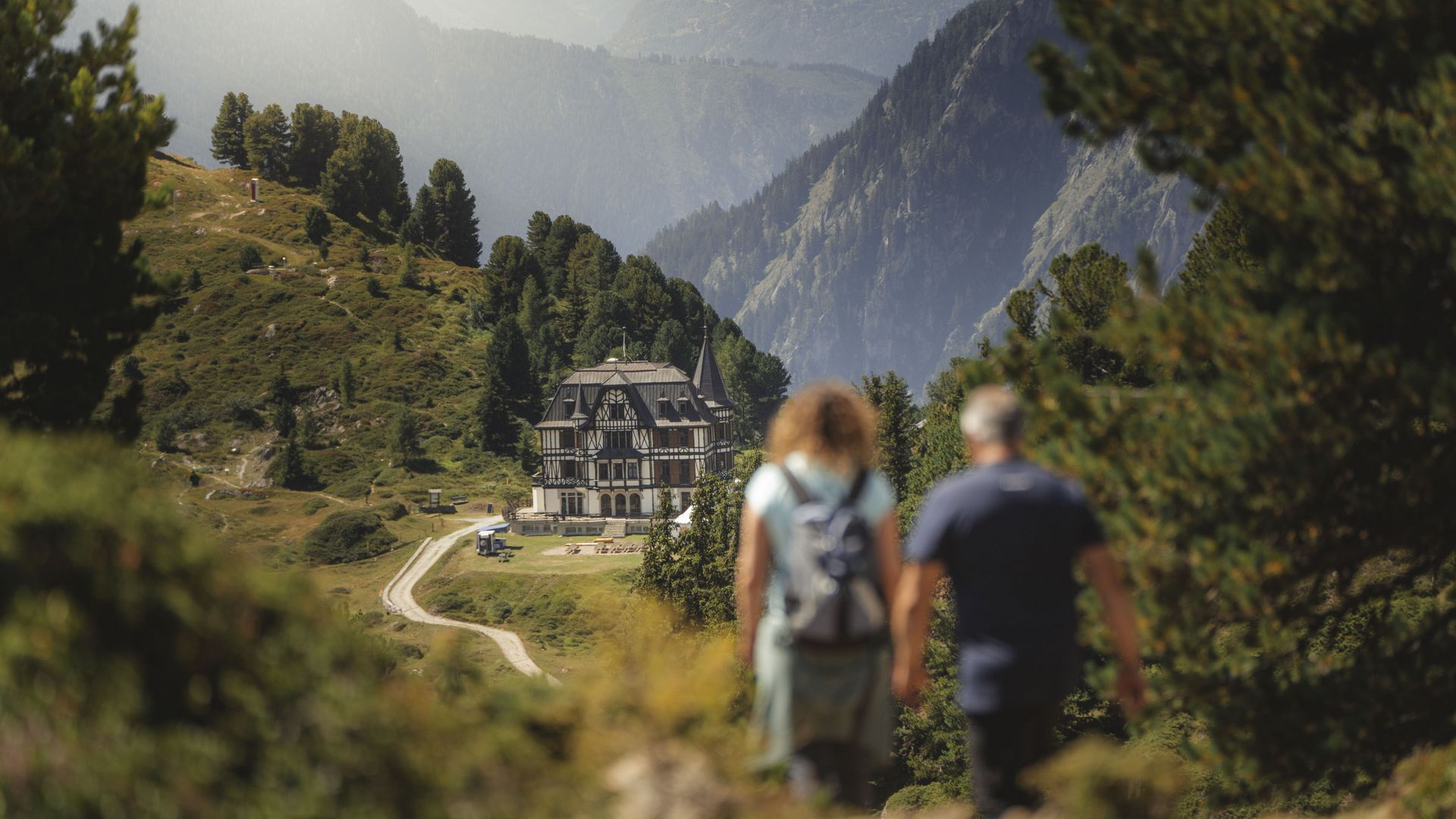 Zwei Wanderer mit Rucksack gehen auf Pfad zur Villa Cassel in der Aletsch Arena umgeben von alpiner Berglandschaft