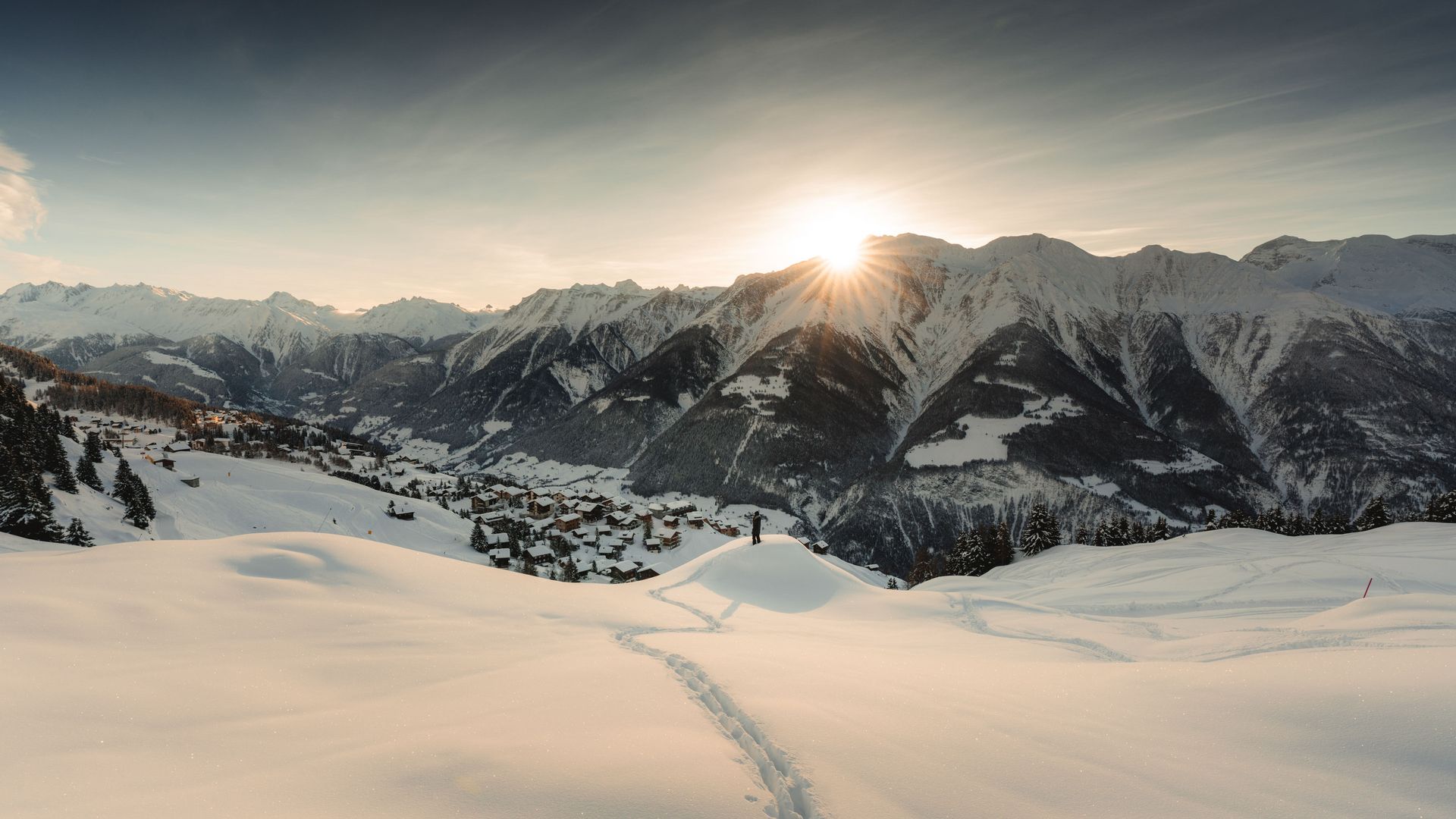 Weihnachten in der Aletsch Arena mit frischer Winterlandschaft, Spur im Schnee und Sonnenaufgang über Bergen bei Riederalp.