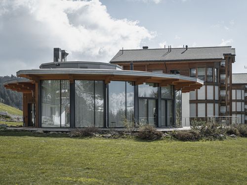 Aussenansicht des runden Holzgebäudes für das Coworking Riederalp mit grossen Panoramafenstern im Sommer.