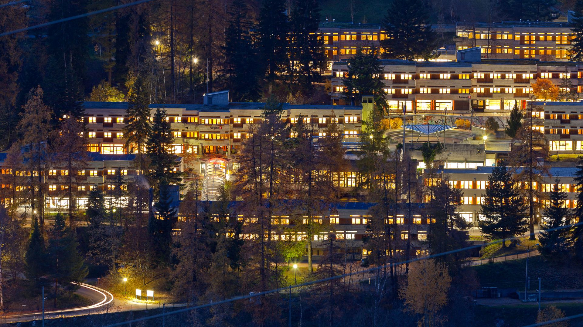 Bâtiments éclairés du Sport Resort à la lisière de la forêt - hébergement idéal pour les offres de groupe Aletsch Arena de nuit.
