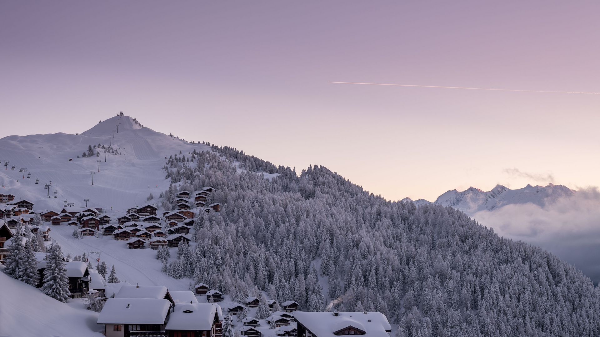 Les chalets enneigés et les pistes de ski de Bettmeralp Suisse devant un coucher de soleil sans nuages, d'un rose tendre.