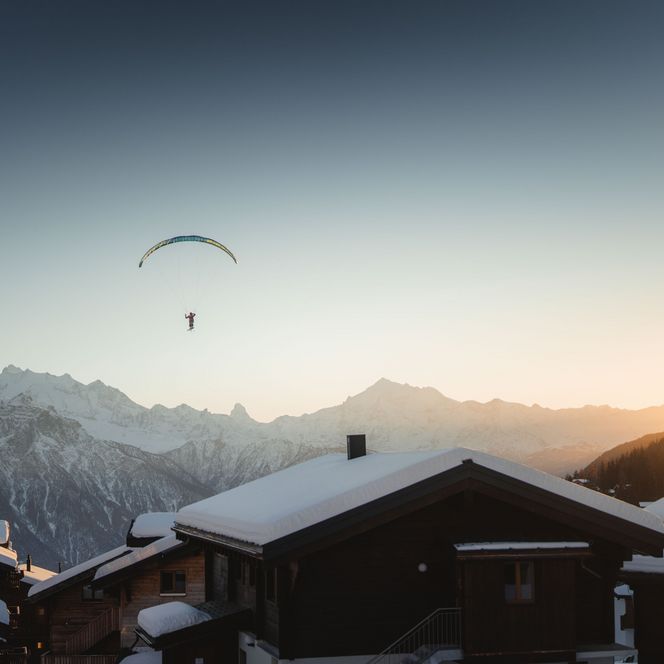 Gleitschirmfliegen hoch über der Bettmeralp vor schneebedeckten Alpen im warmen Sonnenuntergang