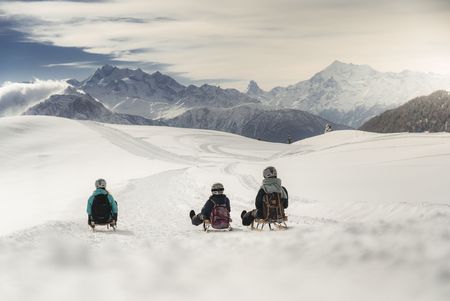 Drei Personen fahren während einem Retreat Aletsch Arena auf Holzschlitten eine verschneite Piste hinunter.
