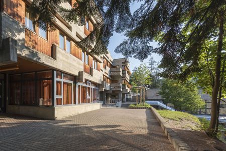 Gebäude des Sport Resort Fiesch mit Holzfassade und Bäumen auf der Seite Nachhaltigkeit Aletsch Arena.
