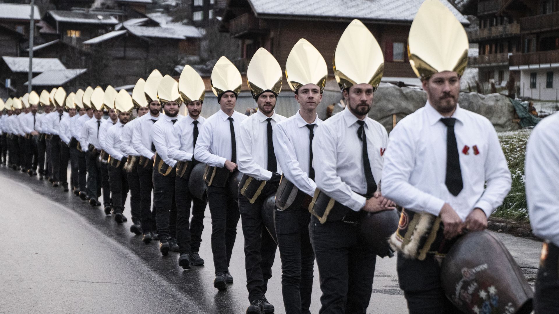 Une rangée d'hommes portant des coiffes dorées et des cloches illustre les traditions hivernales de l'Aletsch Arena.
