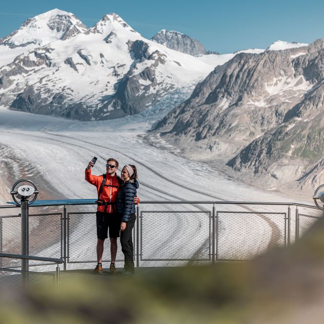 Un couple prend un selfie au point de vue au-dessus de Fiesch Suisse avec le glacier d'Aletsch derrière lui.