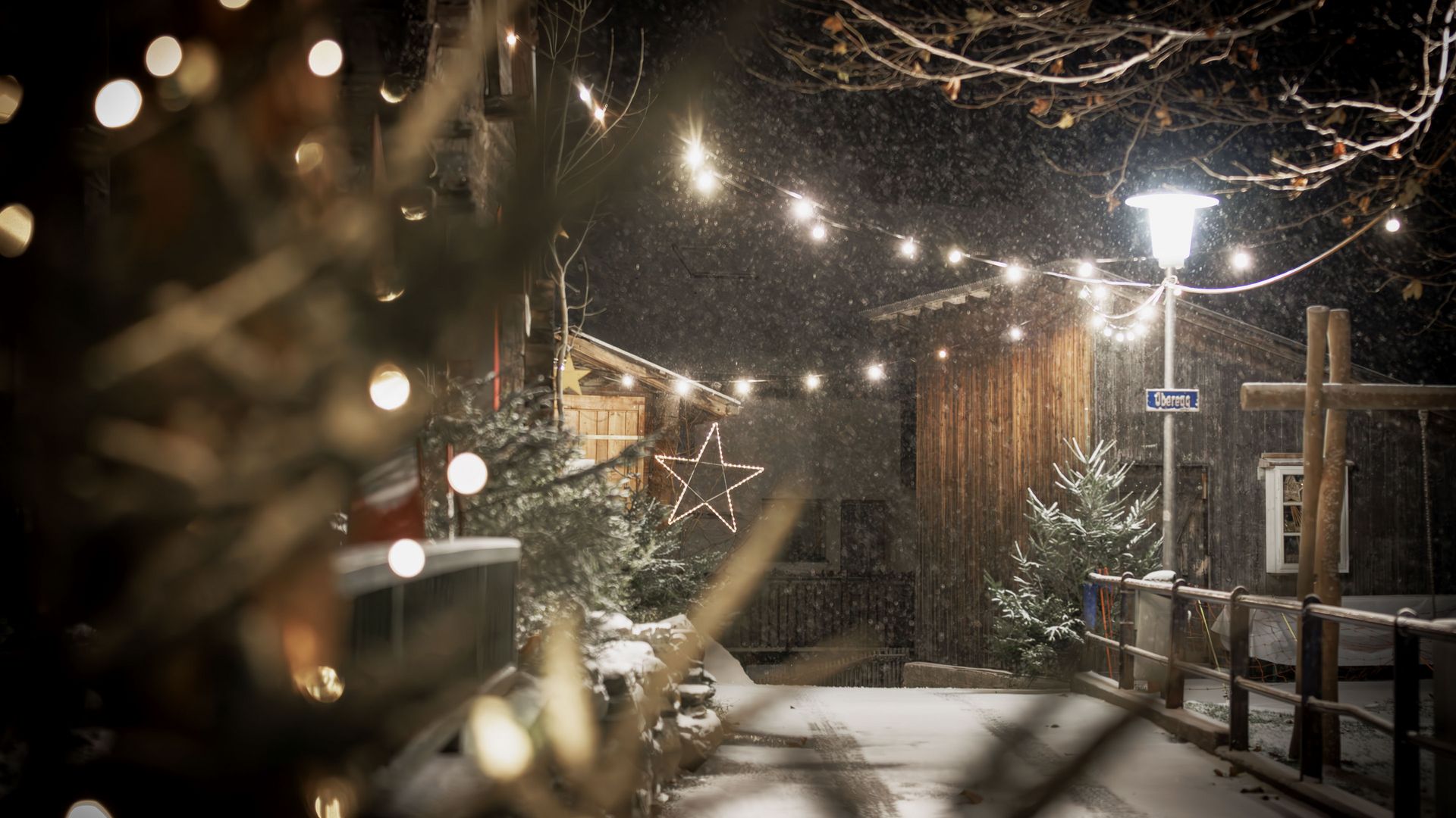 Weihnachten am Gommer Adventsmarkt mit verschneitem Weg, Lichterketten, leuchtendem Stern und festlich dekorierten Holzhäusern bei Nacht.