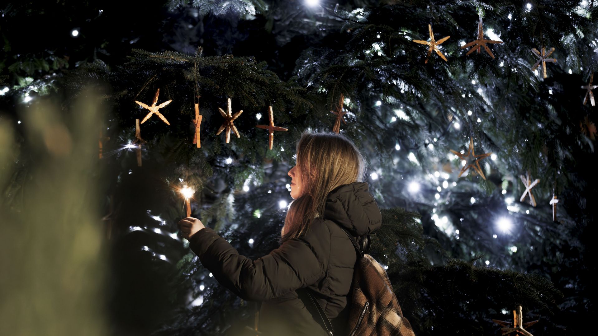 Weihnachten am Gommer Adventsmarkt mit Person, die funkelnde Lichter an einem reich geschmückten Weihnachtsbaum betrachtet.