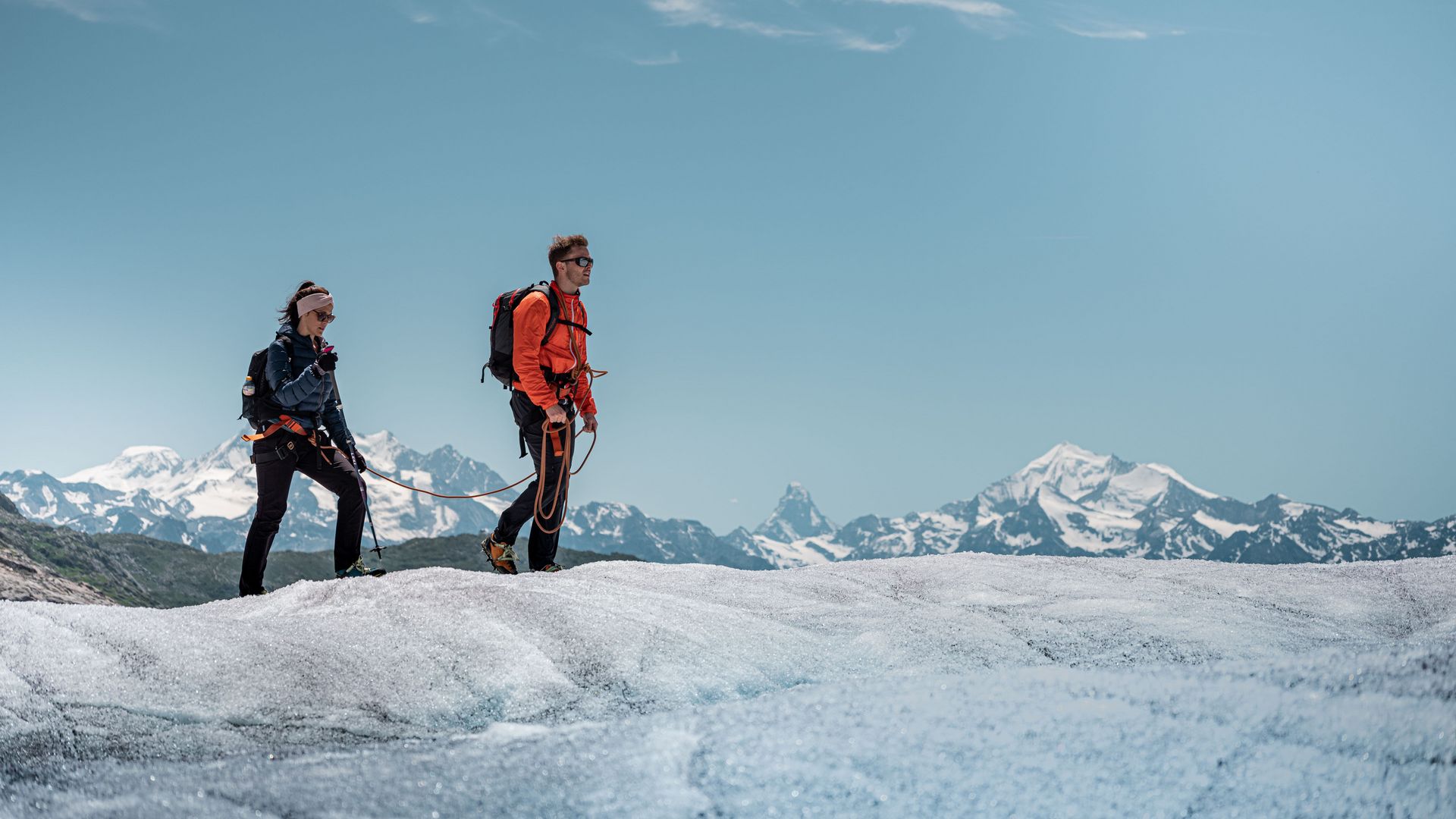 Two people walk on a rope over the white ice on an Aletsch Arena glacier tour, with the Matterhorn towering behind them.