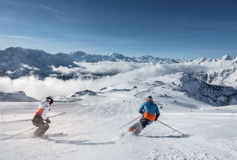 Zwei Skifahrende auf sonniger Piste über den Wolken auf der Seite Auszeichnungen Aletsch Arena.