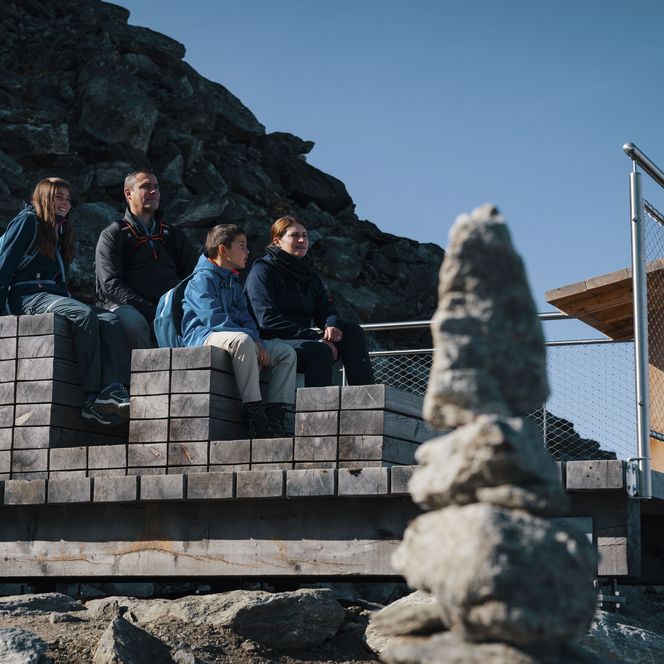 Une famille est assise de manière détendue sur un banc en bois au point de vue ensoleillé au-dessus de Fiesch Suisse.