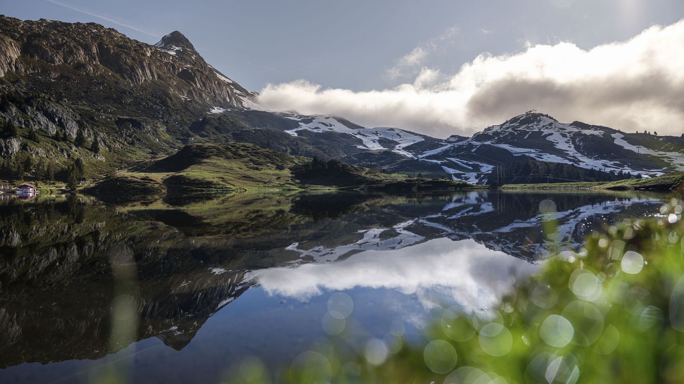 Printemps montagnard dans l'Aletsch Arena avec un lac de montagne tranquille qui reflète clairement les montagnes enneigées et les nuages dans l'eau.