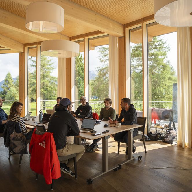 Ein Team sitzt bei einem Retreat Aletsch Arena an einem Tisch in einem hellen, modernen Holzraum mit grossen Fenstern.