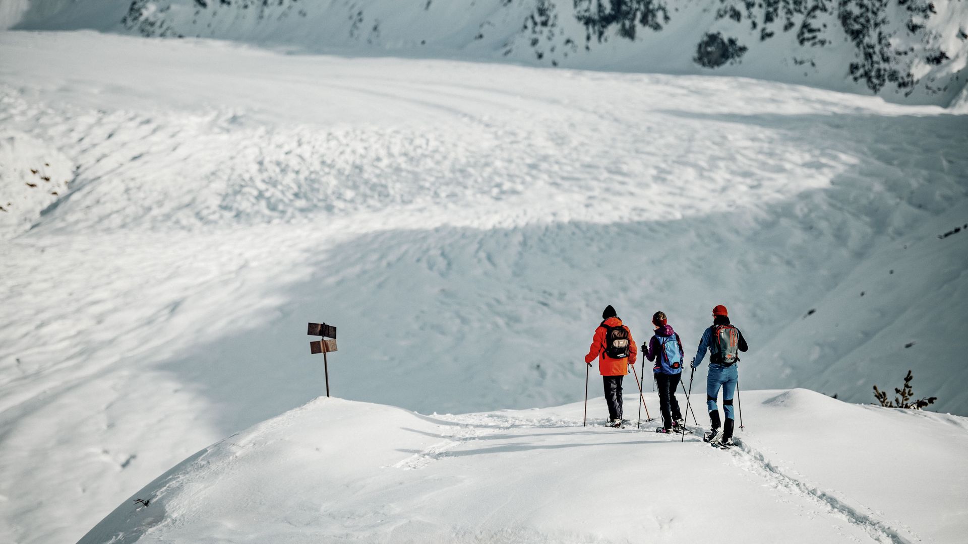 Trois personnes en randonnée à raquettes sur la crête d'Aletsch avec vue sur l'imposant grand glacier d'Aletsch en hiver