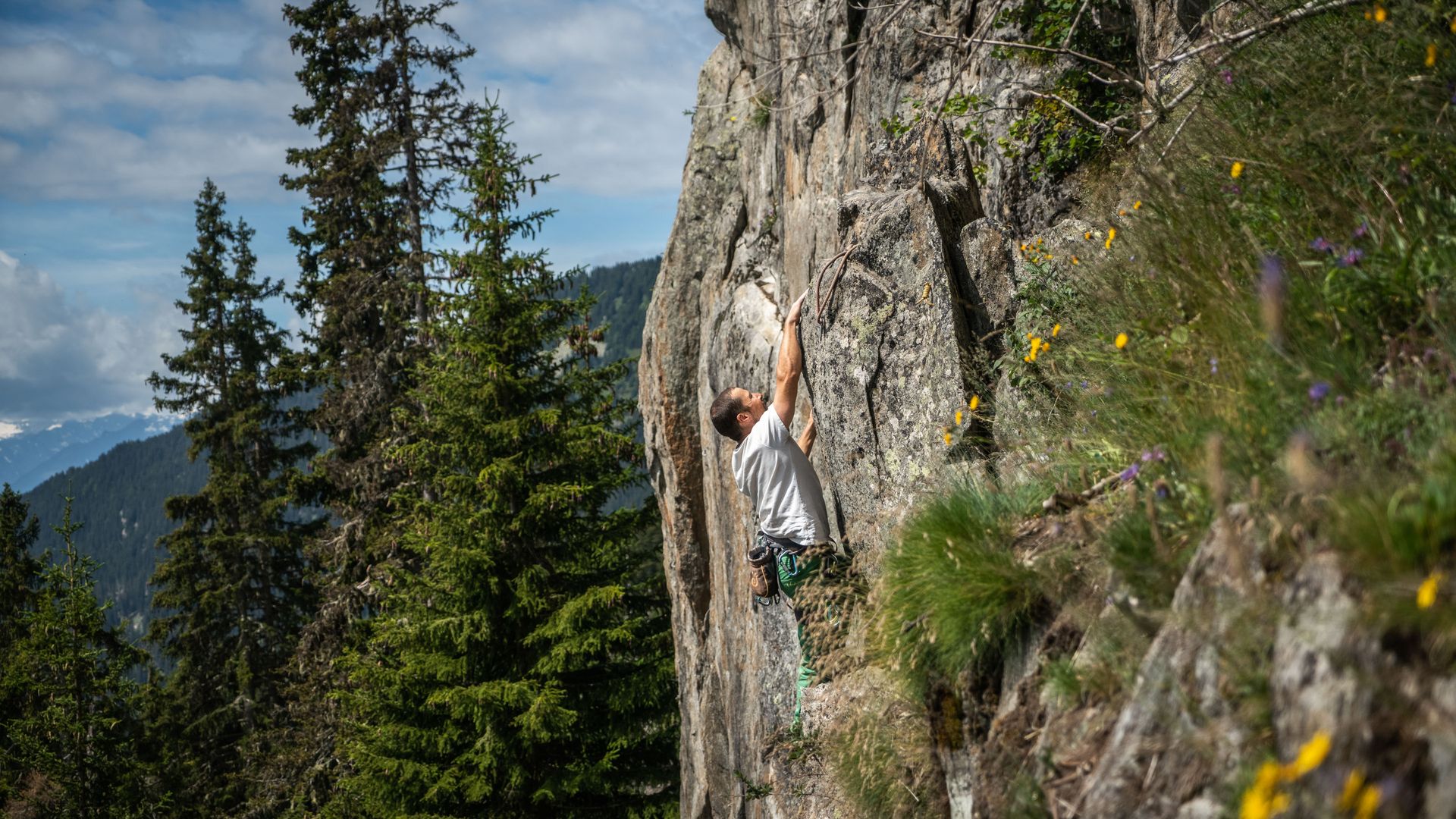 Un grimpeur évolue sur une paroi rocheuse du site d'escalade « Adler » et profite, tout en grimpant, du cadre alpin de l'Aletsch Arena. 