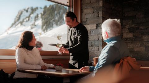Jobs Aletsch Bahnen AG: Serviceperson bringt Gästen im Bergrestaurant Getränke an den Tisch.