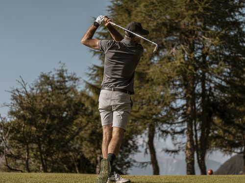 Ein Mann spielt nach seiner Zeit im Coworking Riederalp an einem sonnigen Tag Golf und macht einen Abschlag.