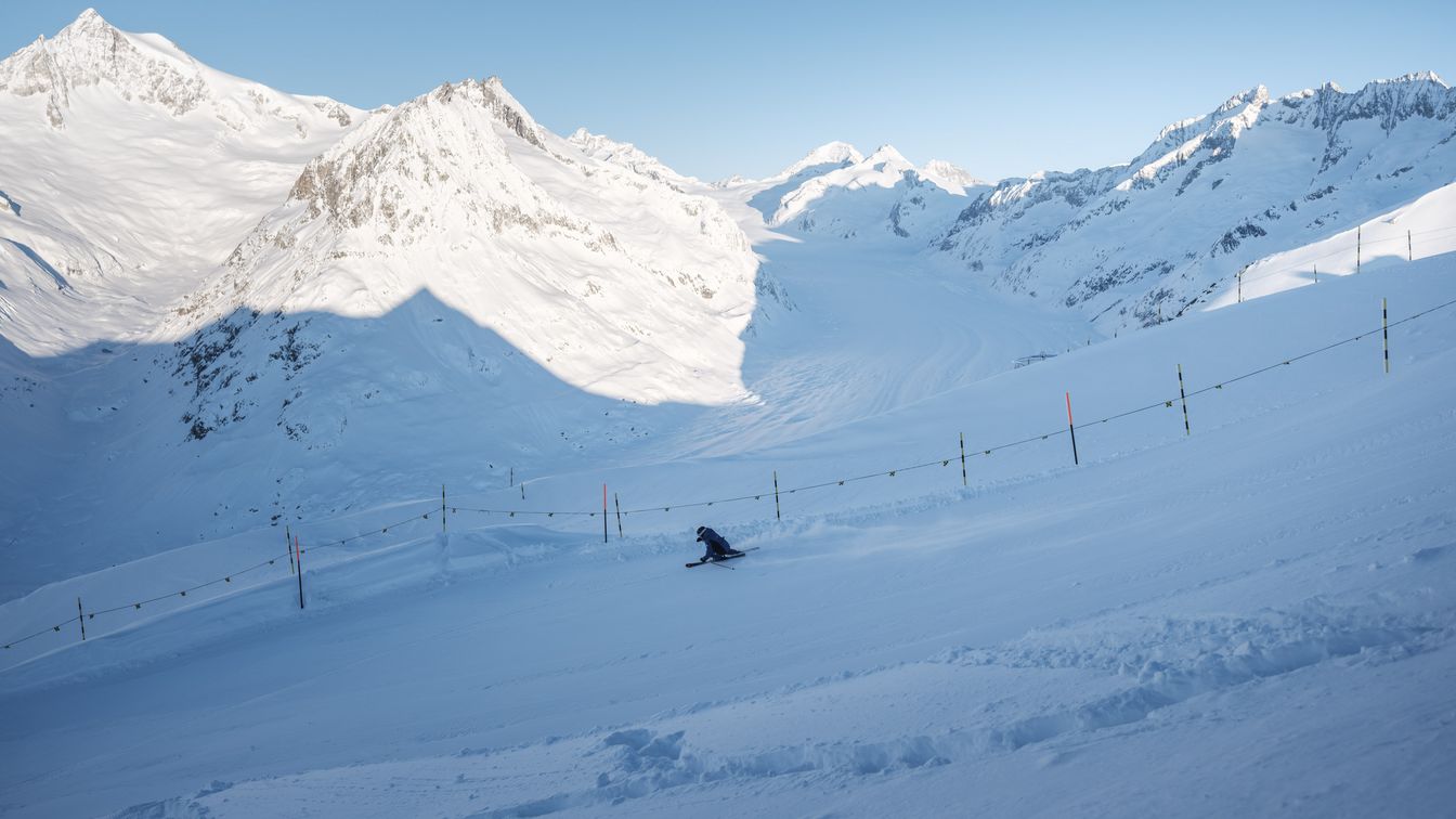 Ein Skifahrer fährt die Piste entlang und geniesst den Blick auf den verschneiten Aletschgletscher