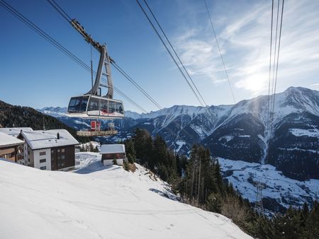 Une télécabine blanche survole les versants de la montagne. Le trajet jusqu'au haut plateau fait partie de l'arrivée et de la mobilité Aletsch Arena.