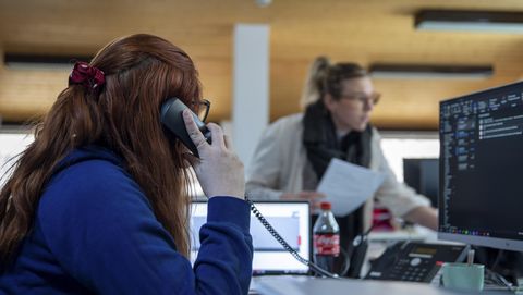 Jobs Aletsch Bahnen AG: Telefonat am Computerarbeitsplatz im Backoffice mit einer zweiten Person im Hintergrund.