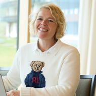 Eine fröhliche Frau im weissen Pullover mit Bärenmotiv sitzt an einem Laptop im modernen Coworking Riederalp.