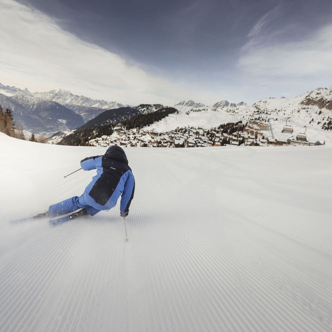 Un skieur descend une piste fraîchement préparée vers un village de montagne enneigé en faisant du ski dans l'Aletsch Arena.