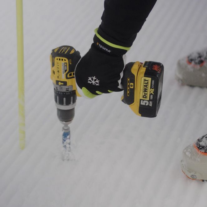 Jobs Aletsch Bahnen AG: Detail der Pistensicherung mit Akkubohrer im Schnee neben einem blauen Absperrnetz.