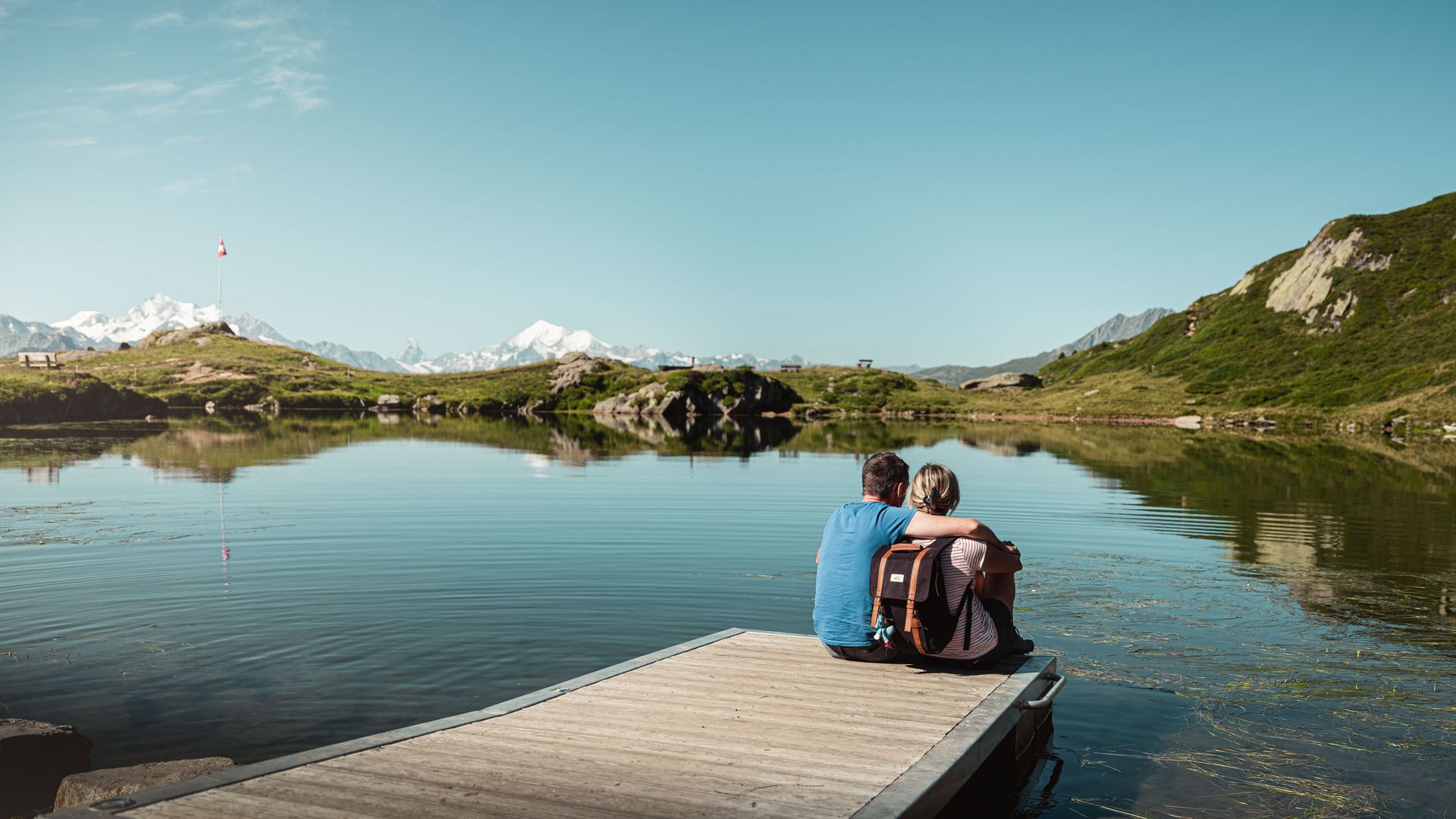 En été, un couple est assis sur une passerelle en bois au bord du paisible lac Blausee à Riederalp, en Suisse, et regarde les montagnes.