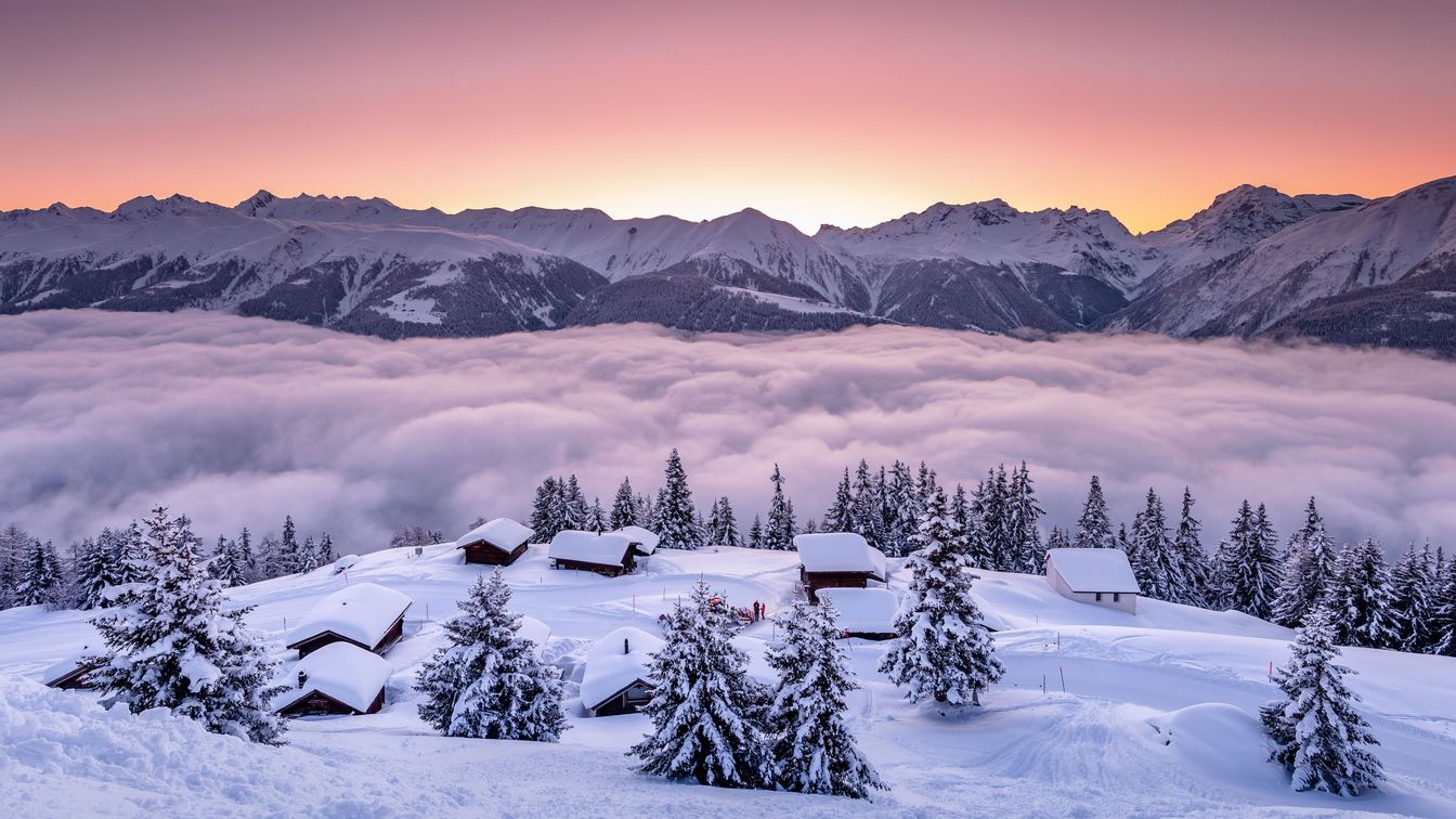 Winterliches Panorama auf der Fiescheralp mit verschneiten Chalets, Tannen und Nebelmeer vor Bergkulisse in der Aletsch Arena