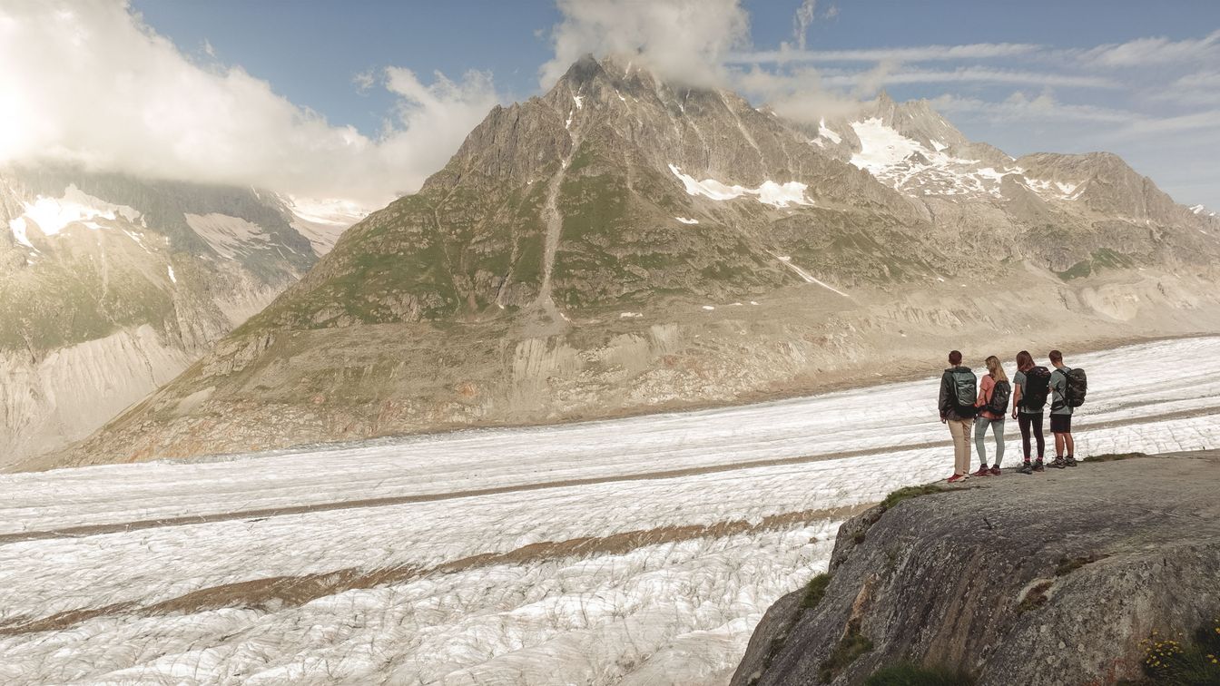 Vier Wanderer stehen am Aussichtspunkt „Platta” und blicken über den Grossen Aletschgletscher