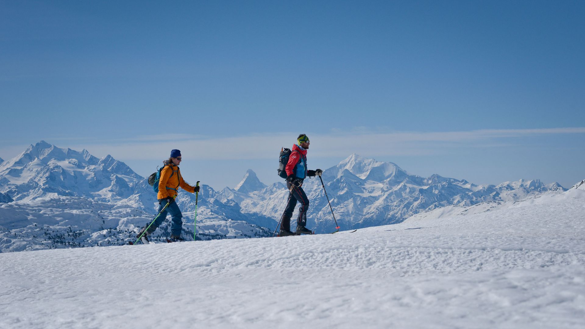 Two people on a ski tour through the snow-covered terrain of the Aletsch Arena, set against a stunning mountain backdrop with a view of the Matterhorn.